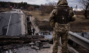 A Ukrainian serviceman looks at a civilian crossing blown up bridge in a village
