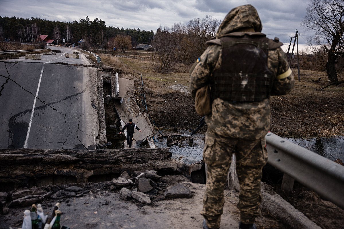 <i>Dimitar Dilkoff/AFP/Getty Images</i><br/>A Ukrainian serviceman looks at a civilian crossing blown up bridge in a village