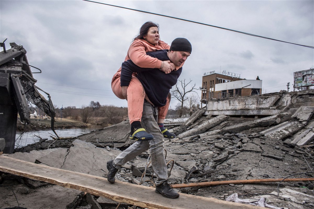 <i>Oleksandr Ratushniak/AP</i><br/>A man carries a woman as they cross an improvised path while fleeing Irpin