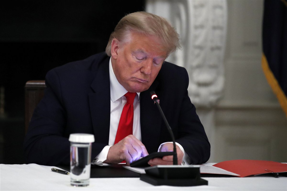 <i>Alex Brandon/AP</i><br/>Former President Donald Trump looks at his phone during a roundtable with governors on the reopening of America's small businesses