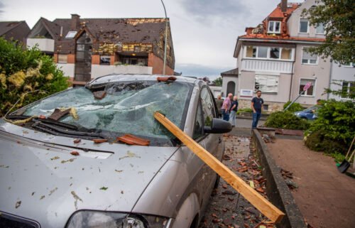 Parts of a roof are seen stuck in the windshield of a parked car.