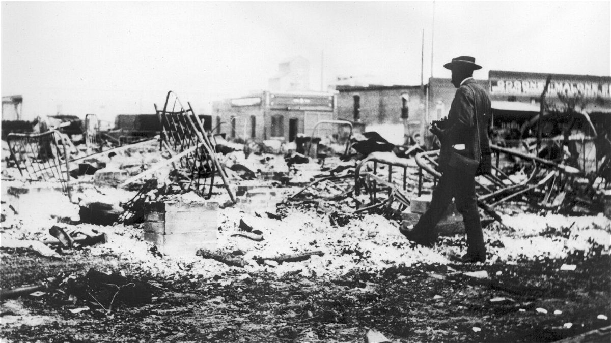 <i>Oklahoma Historical Society/Getty Images</i><br/>An African American man with a camera looking at the skeletons of iron beds which rise above the ashes of a burned-out block after the Tulsa Race Massacre in Tulsa