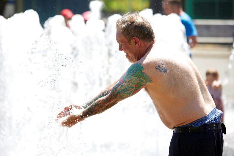 Matthew Carr cools off in the Salmon Street Springs fountain before returning to work cleaning up trash on his bicycle in Portland on Tuesday