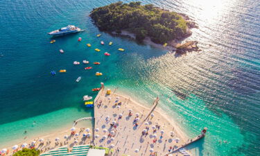 Aerial view of a beautiful white sand beach with turquoise water and relaxing people on a sunny day. Ksamil