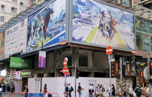 People walk below a billboard ad of fantasy game "Genshin Impact" in Hong Kong