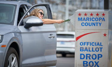 Shana Hofberger leans out of her car door to place her ballot in the ballot drop box outside the Maricopa County Tabulation and Elections Center in Phoenix for Arizona's August 2