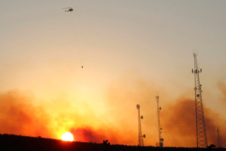 A helicopter carries water on a longline to a wildfire near Salem at sunset Friday