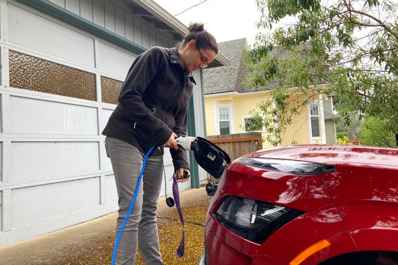 Rebecca DeWhitt charges her electric vehicle in the driveway of the Portland, Ore., home she rents on Sept. 30, 2022. DeWhitt and her partner aren't allowed to use the rental home's garage and so they charge their EV using an extension cord that plugs into a standard electrical outlet outside their front door