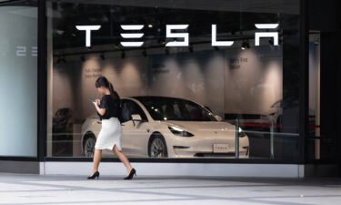 A woman walks past the front window of a Tesla Store in Shinjuku