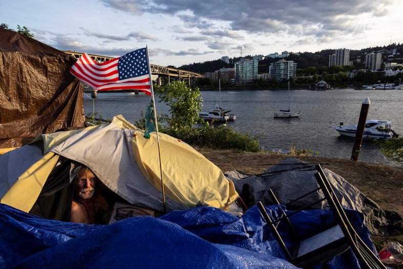 Frank, a homeless man, sits in his tent with a river view in Portland, on June 5, 2021. 