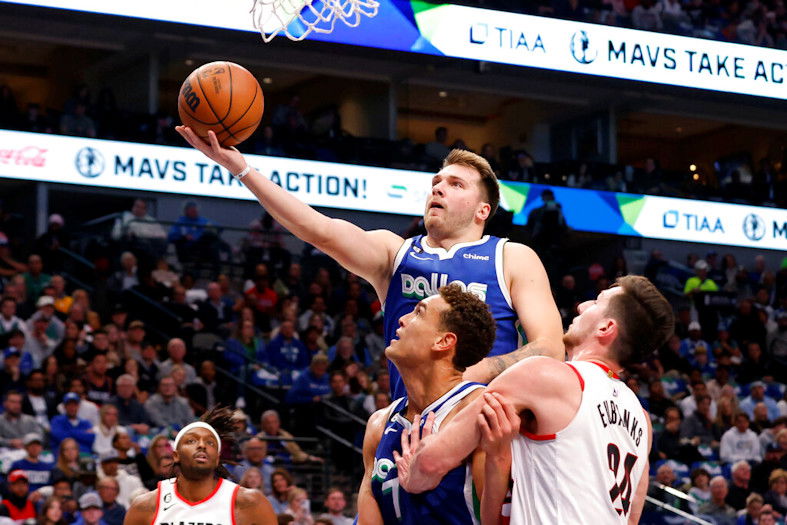 Dallas Mavericks guard Luka Doncic makes a layup next to center Dwight Powell and Portland Trail Blazers forward Drew Eubanks, right, during the first half of an NBA basketball game in Dallas on Saturday