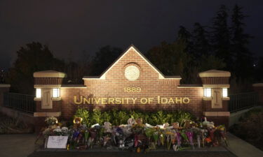 Flowers and other items are displayed at a growing memorial in front of a campus entrance sign for the University of Idaho