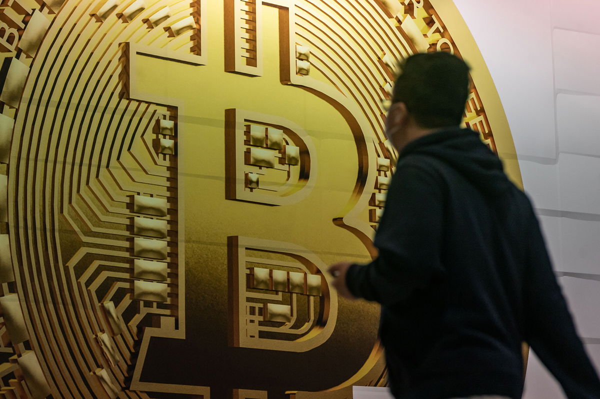 <i>Anthony Kwan/Getty Images</i><br/>Pedestrians walk past an advertisement displaying a Bitcoin cryptocurrency token in February in Hong Kong.