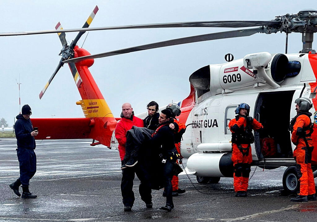  Coast Guard personnel help carry a swimmer from a rescue helicopter after he was rescued from the mouth of the Columbia River after his boat was capsized by a giant wave on Friday