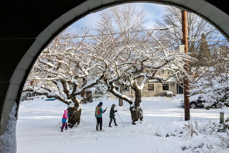 People make their way through a snow-covered street in the Grand Park neighborhood of Portland on Thursday