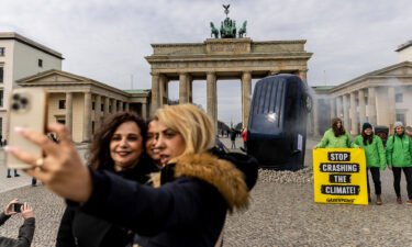People take a selfie with an installation by Greenpeace activists showing an SUV that is seemingly rammed into the pavement in front of the Brandenburg Gate on March 22