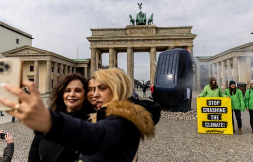 People take a selfie with an installation by Greenpeace activists showing an SUV that is seemingly rammed into the pavement in front of the Brandenburg Gate on March 22
