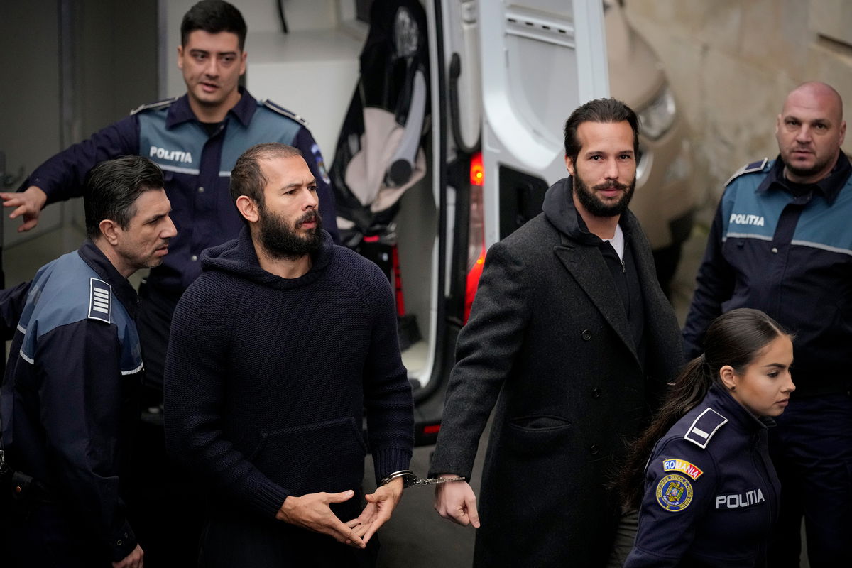 <i>Andreea Alexandru/AP</i><br/>Police officers escort Andrew Tate (center) handcuffed to his brother Tristan Tate