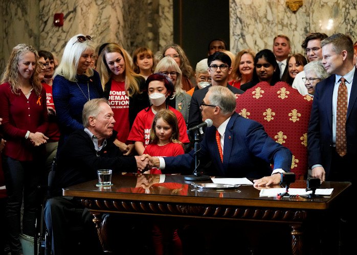 Washington Gov. Jay Inslee shakes the hands of Jim and Ann-Marie Parsons, in blue, whose daughter Carrie was killed in the 2017 Las Vegas shooting, after Inslee signed Senate Bill 5078, which ensures that firearms manufacturers and sellers will face liability if they fail to adopt and implement reasonable controls to prevent sales to dangerous individuals, on Tuesday at the Capitol in Olympia, Wash.