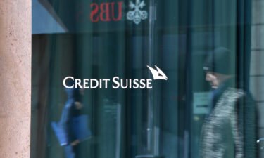 Passersby are reflected in the window of a building of Credit Suisse in Geneva