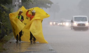 Workers use a tarp to protect themselves from the rain on April 12 in Dania Beach