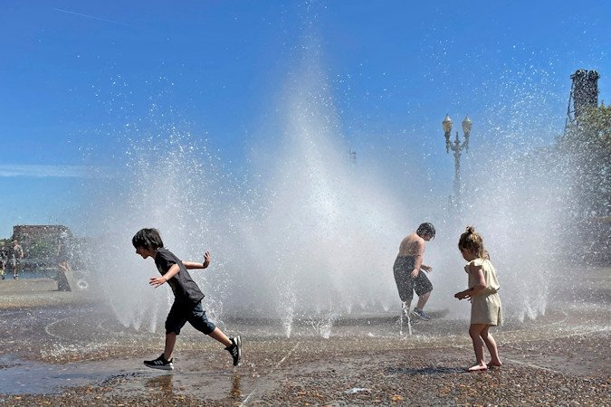 Children play in a fountain to cool off in downtown Portland, Ore., Friday,