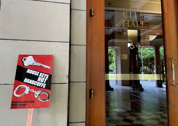 A protest sign condemning a measure in Portland City Council that would ban homeless camps during the daytime in most public places stands next to one of the doors of City Hall in Portland on Wednesday