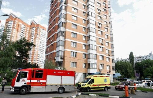 An ambulance and firefighting vehicles are parked outside a multi-storey apartment block following a reported drone attack in Moscow