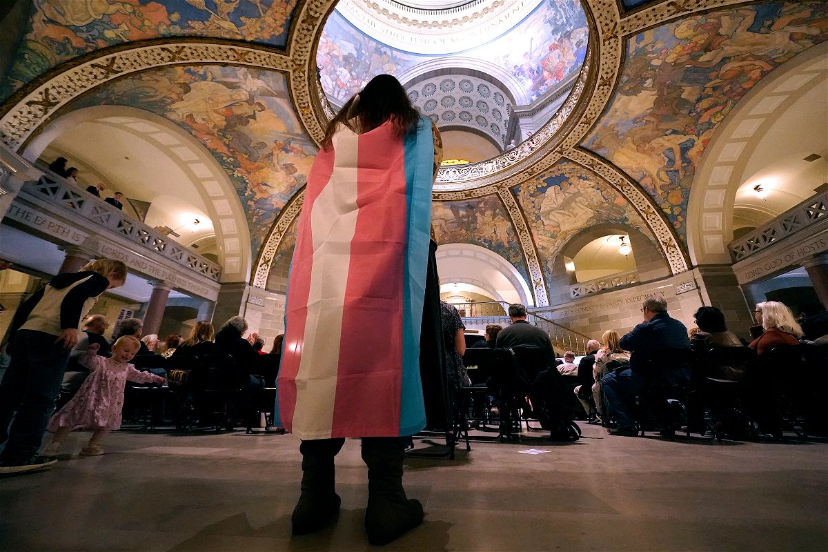 <i>Charlie Riedel/AP</i><br/>Glenda Starke wears a transgender flag as a counterprotest during a rally in favor of a ban on gender-affirming health care legislation on March 20
