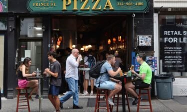 People eat at tables on the sidewalk outside Prince St. Pizza on June 25 in New York City.