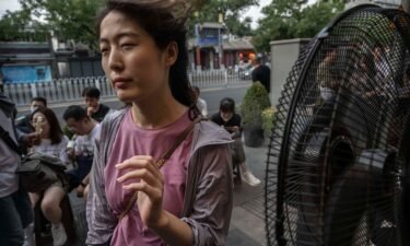 A woman cools herself on a misting fan as she waits for a table outside a popular local restaurant during a heatwave on June 23