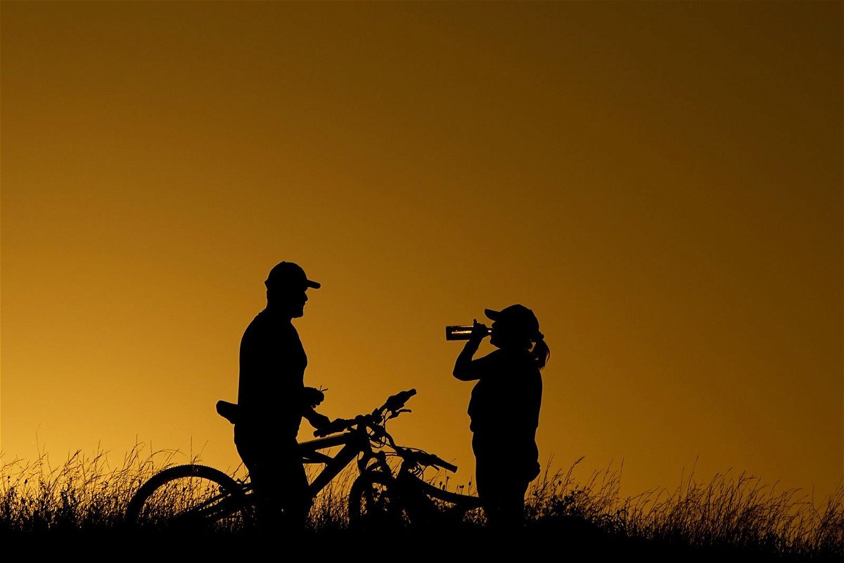 <i>Eric Gay/AP</i><br/>Cyclists take a water break on a June 2023 evening ride during a heat wave in San Antonio.