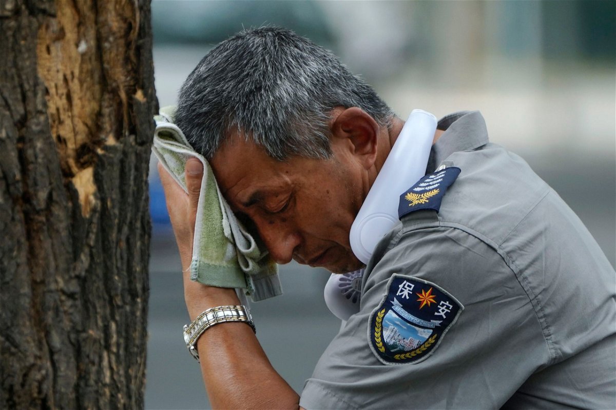 <i>Andy Wong/AP</i><br/>A security guard wearing an electric fan on his neck wipes his sweat on a hot day in Beijing