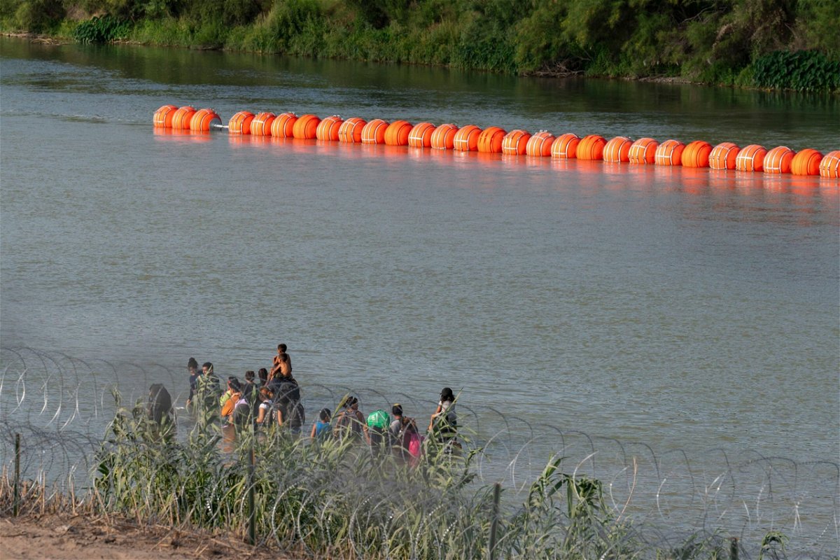 <i>Suzanne Cordeiro/AFP/Getty Images</i><br/>Migrants walk by a string of buoys placed on the water along the Rio Grande border with Mexico in Eagle Pass