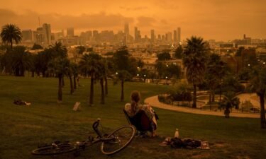 A person sits in Delores Park as smoke and fog hang over the skyline in San Francisco
