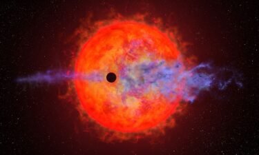 This artist's illustration shows the shadow of a planet passing in front of the red dwarf star AU Microscopii. Blue clouds depict the planet's atmosphere