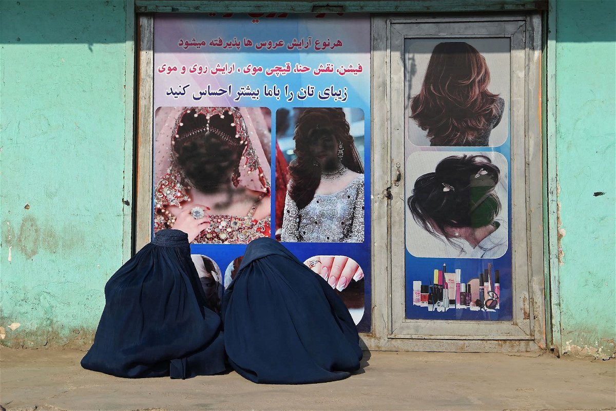 <i>Wakil Kohsar/AFP/Getty Images</i><br/>Afghan burqa-clad women sit in front of a beauty salon with images of women defaced using spray paint in Jalalabad on December 13