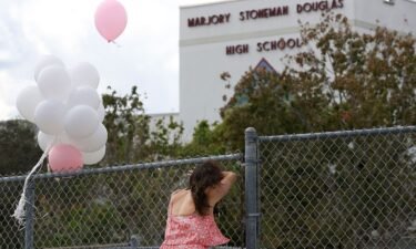 A person rests against the fence that surrounds the Marjory Stoneman Douglas High School
