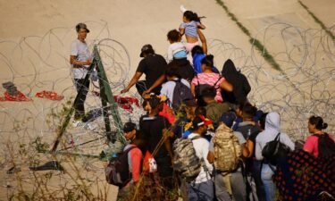 Migrants cross a razor wire fence near a border wall on the banks of the Rio Grande