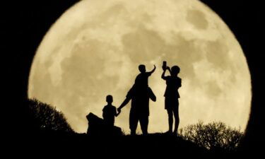 A family stand with the full moon known as the "Sturgeon Moon" in the background