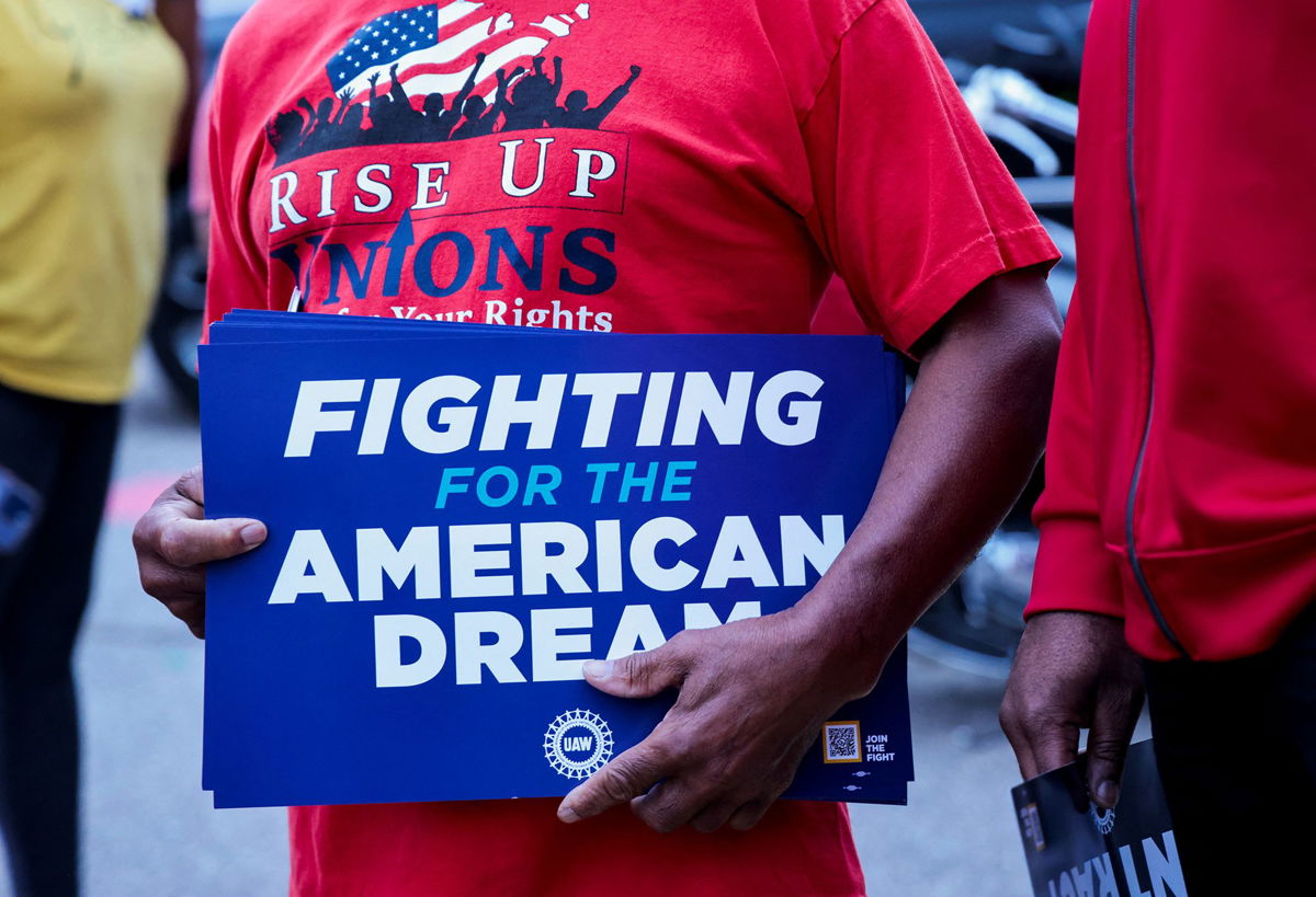 <i>Rebecca Cook/Reuters</i><br/>A United Auto Workers union member holds a sign outside Stellantis Sterling Heights Assembly Plant