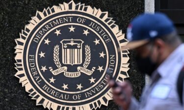 A pedestrian walks past a seal reading "Department of Justice Federal Bureau of Investigation"