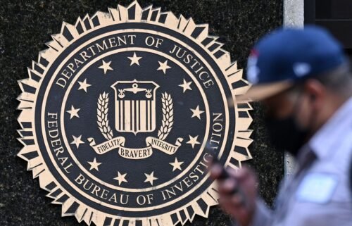A pedestrian walks past a seal reading "Department of Justice Federal Bureau of Investigation"