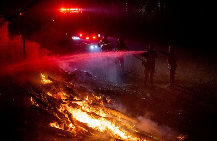 Firefighters douse flames while battling a wildfire called the Highland Fire in Aguanga, California, on Monday, October 30