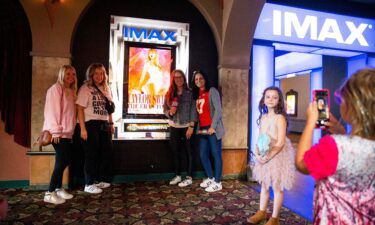 A young Taylor Swift fan takes a photo of the moms of their group next to the "Taylor Swift: The Eras Tour" poster before they go in to see the movie at Malco Paradiso Cinema Grill and IMAX in Memphis