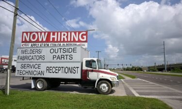 A Now Hiring sign advertising job openings is viewed outside a Truck dealership