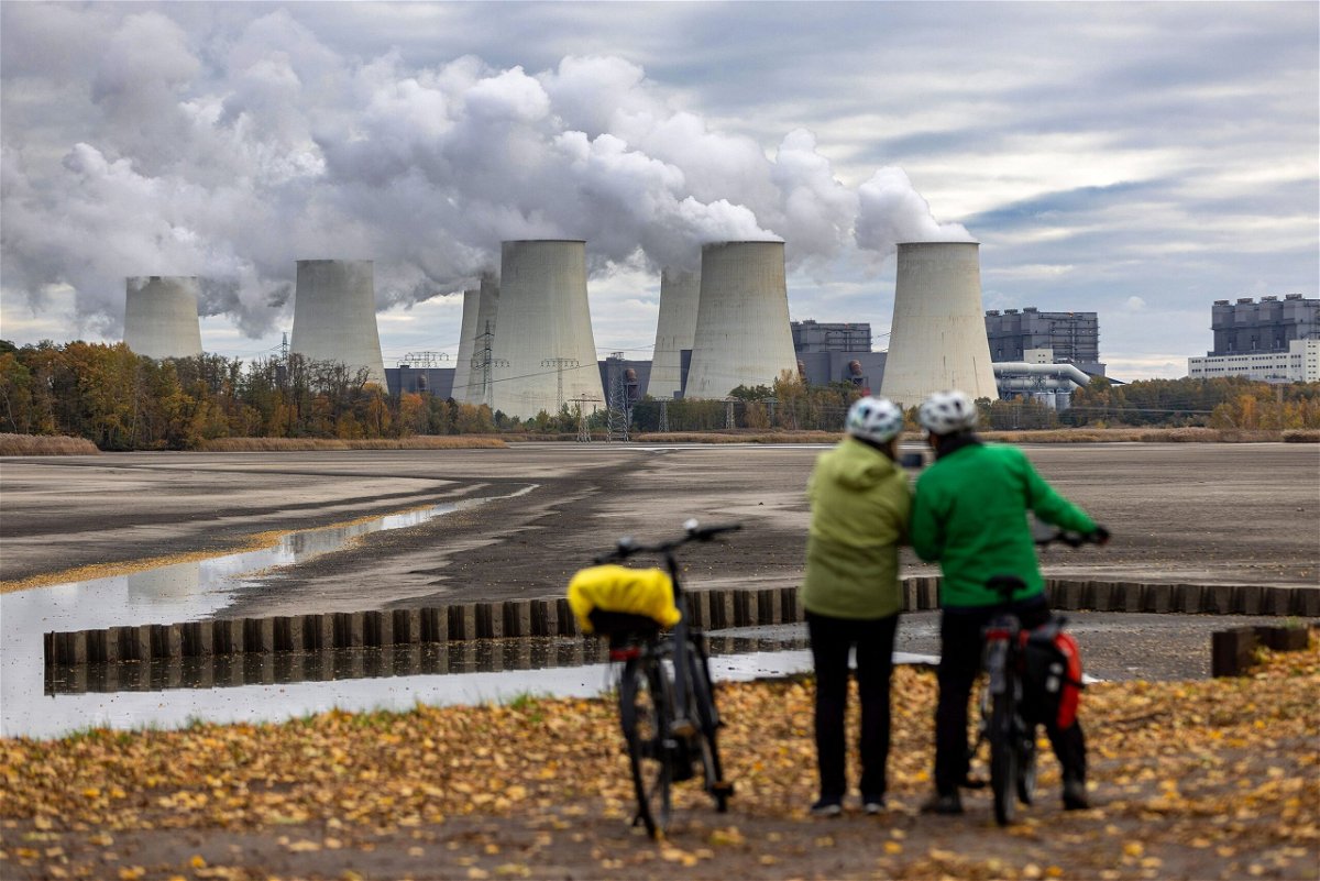 <i>Krisztian Bocsi/Bloomberg/Getty Images</i><br/>Cyclists look towards cooling towers at the Jaenschwalde lignite coal-fired power plant