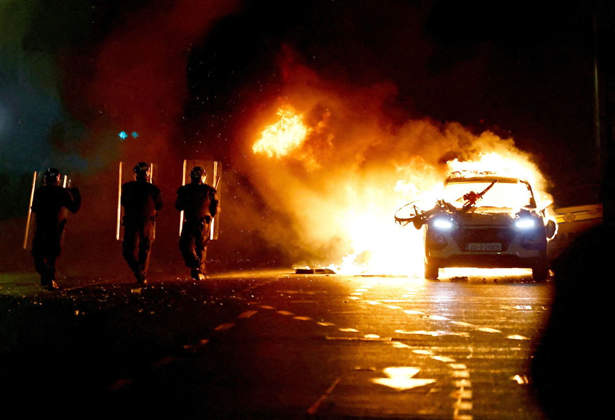 <i>Clodagh Kilcoyne/Reuters</i><br/>Riot police walks next to a burning police vehicle