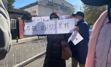 Family members of passengers on board flight MH370 hold up signs demanding an open trial near a court in Beijing's Chaoyang district during a closed-door hearing on November 27.