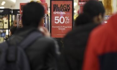 People walk past advertised Black Friday discount signs at the Macy's retail store inside the Queens Center Mall